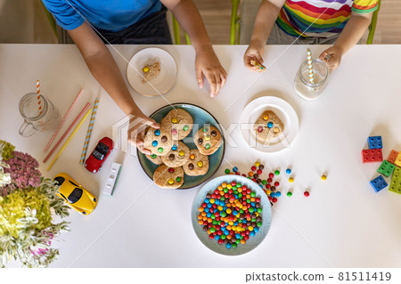 Funny male brothers eat cookies with round multi-colored sweets m&m and drink milk. Top view. 81511419