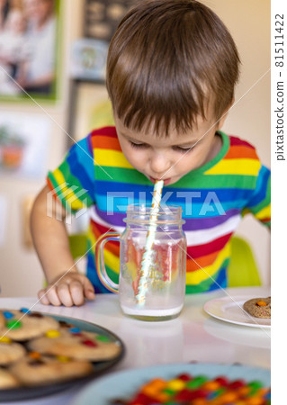 Funny boy eat cookies with round multi-colored sweets m&m and drink milk. 81511422