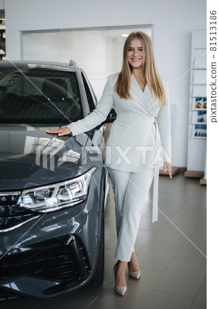 Portrait of gorgeous woman in showroom. Beautiful salesperson standing by car. Blond hair female after buying car Portrait of gorgeous woman in showroom. Beautiful salesperson standing by car. Blond hair female after buying car 81513186