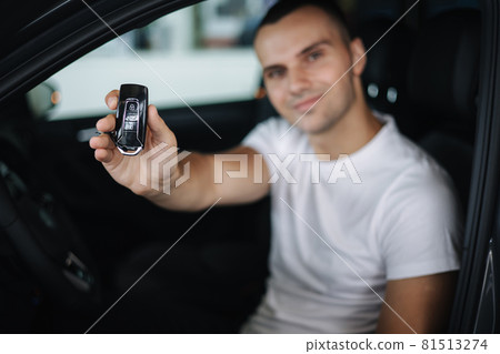 Man sitting in his new car in car showroom. Portrait of handsome man in car hold keys in hands. Keys in focus 81513274