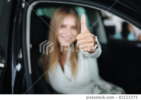 Attactive young bussines woman sitting in car in car showroom. Woman choosing new car. Beautiful blond hair female in suit. Woman defocused 81513373