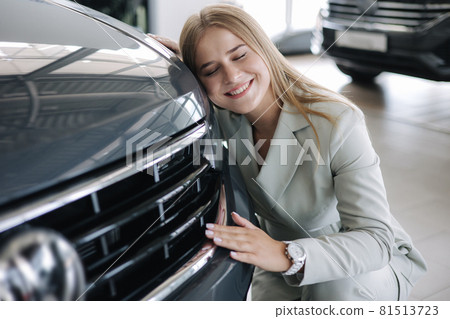 Business woman chossing a new car in a car showroom. Happy female hug new car and very glad Business woman chossing a new car in a car showroom. Happy female hug new car and very glad 81513723
