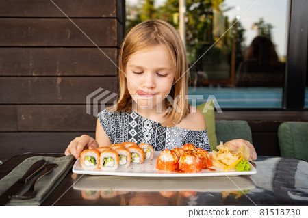 little girl in cafe, restaurant, country house smiles and licks looks Asian Japanese sushi rolls little girl in cafe, restaurant, country house smiles and licks looks Asian Japanese sushi rolls 81513730