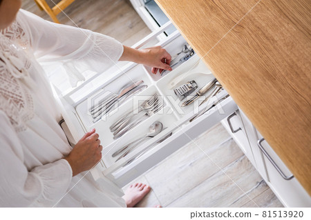 Closeup female hands neatly assembling cutlery in storage pp boxes at drawer of minimalistic kitchen Closeup female hands neatly assembling cutlery in storage pp boxes at drawer of minimalistic kitchen 81513920