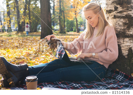 A young woman works in a park, typing on a laptop 81514336