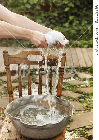 Woman washing dirty clothing in metal basin with foam water on sunny day near home 81515866