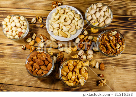 Assortment of nuts on wooden table. Almond, hazelnut, pistachio, peanut, walnut and cashew in small bowls. Top view. Healthy eating concept Assortment of nuts on wooden table. Almond, hazelnut, pistachio, peanut, walnut and cashew in small bowls. Top view. Healthy eating concept 81516188
