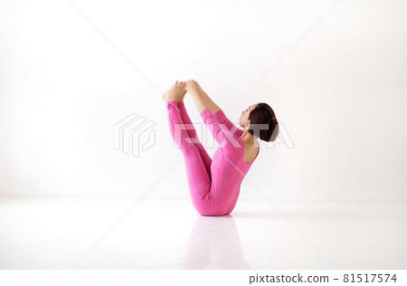 Young slender woman in pink long bodysuit performing yoga Boat Navasana pose 81517574