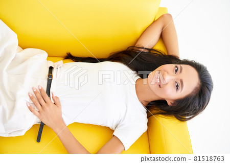 Top view of smiling pretty asian woman relaxing on yellow sofa Top view of smiling pretty asian woman relaxing on yellow sofa 81518763