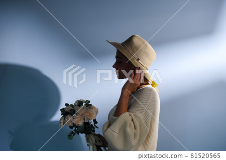 A young beautiful blonde caucasian woman with a short haircut in a beige suit and hat with bouquet of white flowers on blue background. Beauty portrait. The girl smiles, clean skin and white teeth. A young beautiful blonde caucasian woman with a short haircut in a beige suit and hat with bouquet of white flowers on blue background. Beauty portrait. The girl smiles, clean skin and white teeth. 81520565