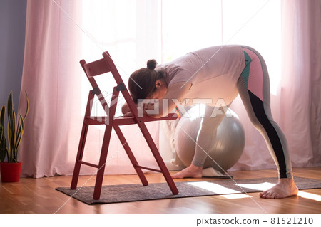Pregnant woman doing inversion Standing Intense Spread Leg Prasarita Padottanasana yoga pose at home 81521210