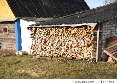 Chopped logs of firewood piled under the roof in the village  in a backyard.  81522164