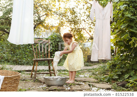 Little girl in dress washing clothes in metal basin while helping mom with chores in backyard Little girl in dress washing clothes in metal basin while helping mom with chores in backyard 81522538