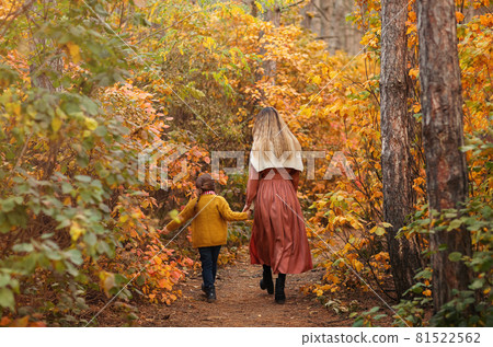Rear view or young family, mother and little son, on walk in autumn forest, mom and child holding hands and walking along path covered with yellow tree leave Rear view or young family, mother and little son, on walk in autumn forest, mom and child holding hands and walking along path covered with yellow tree leave 81522562