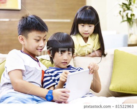 three asian children sitting on couch at home playing video game using digital tablet 81522963