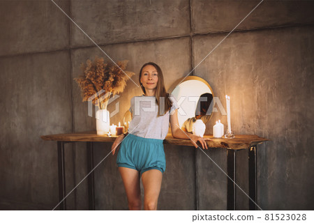 Beautiful slim middle-aged woman in homewear leaning on dressing wooden table with round mirror Beautiful slim middle-aged woman in homewear leaning on dressing wooden table with round mirror 81523028