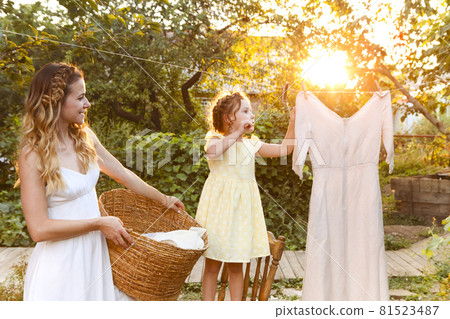 Mother and daughter hanging laundry in backyard 81523487