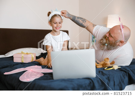Daddy adjusts headband on head of little girl watching video on large bed at home 81523715