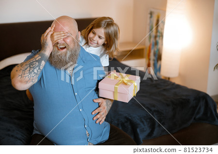Little girl with present closes father eyes to make surprise at holiday in bedroom 81523734