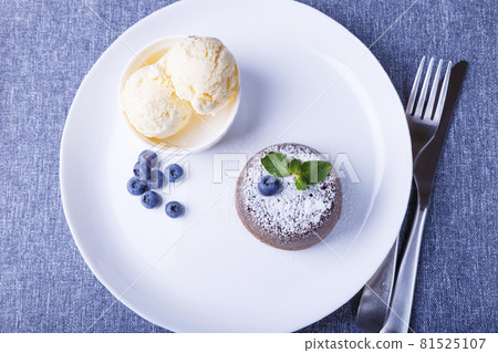 Lava cake - chocolate fondant cake with vanilla ice cream, blueberries and mint. Traditional French pastries. Close-up, top view. Lava cake - chocolate fondant cake with vanilla ice cream, blueberries and mint. Traditional French pastries. Close-up, top view. 81525107