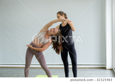 A young caucasian woman is teaching yoga stretching pose to her friend at home A young caucasian woman is teaching yoga stretching pose to her friend at home 81525463