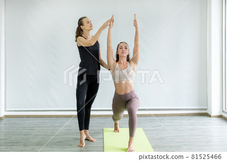 A young caucasian woman is teaching yoga stretching pose to her friend at home A young caucasian woman is teaching yoga stretching pose to her friend at home 81525466