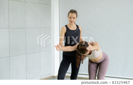 A young caucasian woman is teaching yoga stretching pose to her friend at home A young caucasian woman is teaching yoga stretching pose to her friend at home 81525467