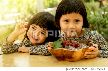 Happy baby and kid wearing twin clothes sitting on the table with a plate of grapes freeze in ice, eat healthy fruit childhood lifestyle Happy baby and kid wearing twin clothes sitting on the table with a plate of grapes freeze in ice, eat healthy fruit childhood lifestyle 81525471