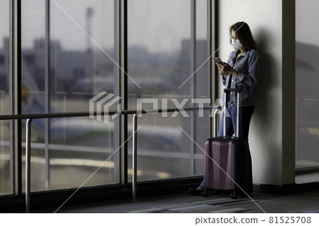 Beautiful Asian traveler wearing hygiene protective mask standing alone and using a smartphone at the airport while waiting for a flight. Idea for traveling in a new normal situation Beautiful Asian traveler wearing hygiene protective mask standing alone and using a smartphone at the airport while waiting for a flight. Idea for traveling in a new normal situation 81525708