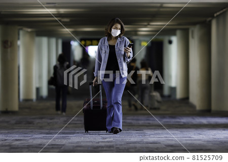 Beautiful Asian traveler wearing hygiene protective mask holding luggage bag walking and using smartphone in the airport terminal. Idea for a new normal traveling Beautiful Asian traveler wearing hygiene protective mask holding luggage bag walking and using smartphone in the airport terminal. Idea for a new normal traveling 81525709
