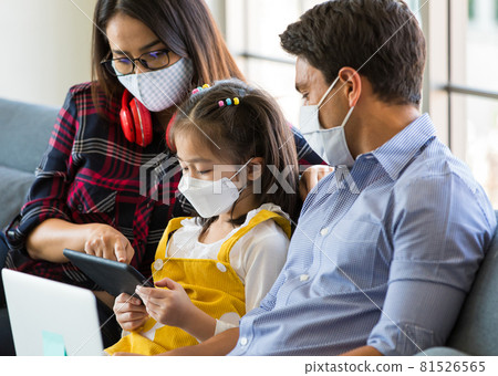Mixed race family stays at home together with wearing protective hygiene mask on faces, father and mother helping and teaching little girl to use tablet computer in learning Mixed race family stays at home together with wearing protective hygiene mask on faces, father and mother helping and teaching little girl to use tablet computer in learning 81526565