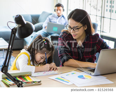 Muti ethnic family, father, and mother and young little daughter stay together in living room. Mom work from home with laptop notebook computer while teaching girl to do homework. New normal concept 81526568