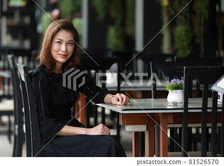 Beautiful cute Asian woman in black dress sitting alone in outdoor food shop and looking to camera Beautiful cute Asian woman in black dress sitting alone in outdoor food shop and looking to camera 81526570