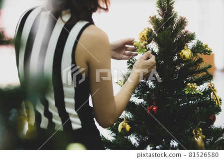 Back view of woman decorating and arranging Christmas tree at home and preparing for winter holidays with calm circumstance Back view of woman decorating and arranging Christmas tree at home and preparing for winter holidays with calm circumstance 81526580