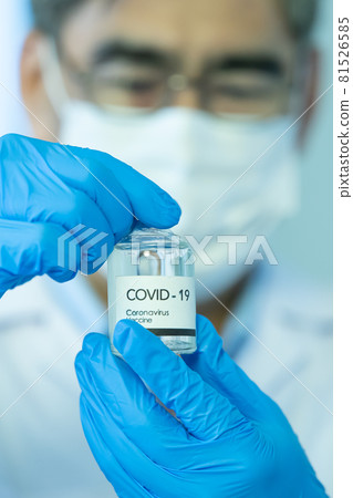 Hand of doctor or researcher in medical blue gloves holding and pointing to a bottle of COVID-19 coronavirus vaccine Hand of doctor or researcher in medical blue gloves holding and pointing to a bottle of COVID-19 coronavirus vaccine 81526585