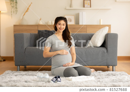 Happy Pregnant Woman sit on carpet in front of sofa and stroking big belly with baby stuff prepare for love at cozy home,Pregnancy of young woman enjoy with future life,Motherhood and Pregnant Concept Happy Pregnant Woman sit on carpet in front of sofa and stroking big belly with baby stuff prepare for love at cozy home,Pregnancy of young woman enjoy with future life,Motherhood and Pregnant Concept 81527688