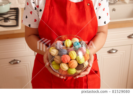 Woman in red apron holding glass bowl with sweets Woman in red apron holding glass bowl with sweets 81529080