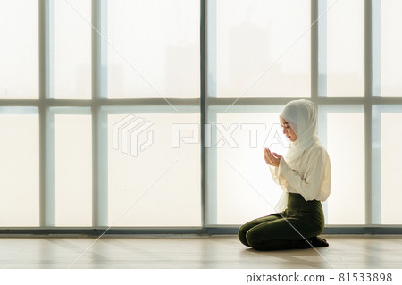 Young and beautiful Asian Muslim woman sitting on floor and praying with respect and calm manner Young and beautiful Asian Muslim woman sitting on floor and praying with respect and calm manner 81533898