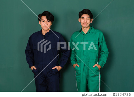 portrait of two smart and handsome young Asian men dressed in blue and green mechanic coveralls stand confidently with crossed arms over green background portrait of two smart and handsome young Asian men dressed in blue and green mechanic coveralls stand confidently with crossed arms over green background 81534726