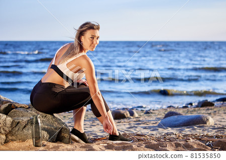 Woman is sitting near coast as rest during running. 81535850