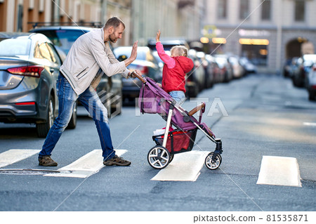 Man plays with little daughter in baby carriage on crosswalk near traffic. Man plays with little daughter in baby carriage on crosswalk near traffic. 81535871