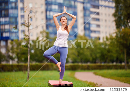 Happy woman makes yoga training on park bench. 81535879