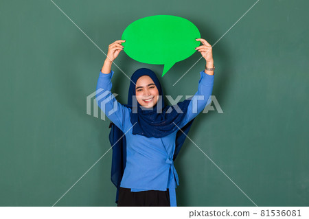 confident and happy woman concept. Pretty attractive Muslim lady dressed beautifully wearing blue hijab standing and holding green blank speech bubble over green background 81536081