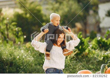 Mother and son sitting on a garden near many pumpkins 81538262