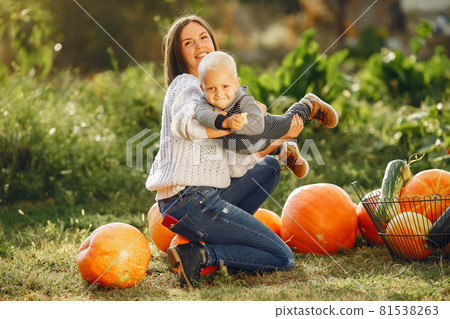 Mother and son sitting on a garden near many pumpkins 81538263