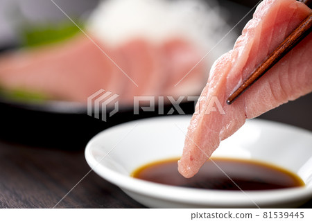 Close-up of tuna sashimi soaked in soy sauce on a small plate with chopsticks 81539445