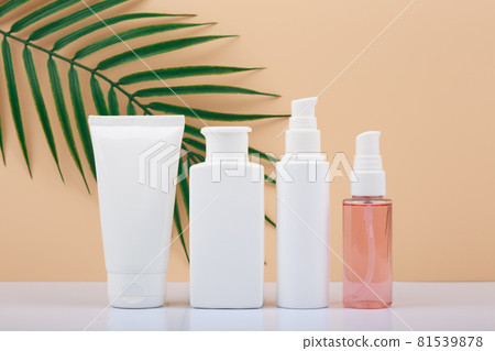 Cosmetic bottles in a row against bright beige background with palm leaf 81539878
