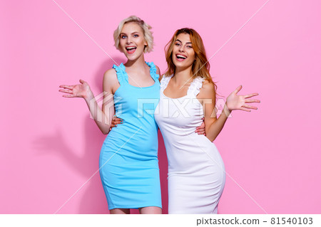 Two stunning beautiful confident lady chic hugging wearing pretty nice cute dresses isolated on pink studio background 81540103