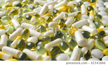 The pills are scattered on the table. Tablets on the green background. Medicinal tablets, capsules. 81541666