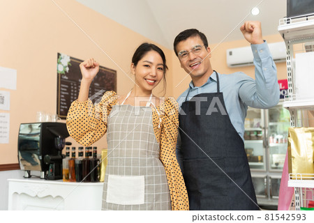 Cheerful business owners standing welcomingly together in front of the counter of their cafe. Cheerful business owners standing welcomingly together in front of the counter of their cafe. 81542593